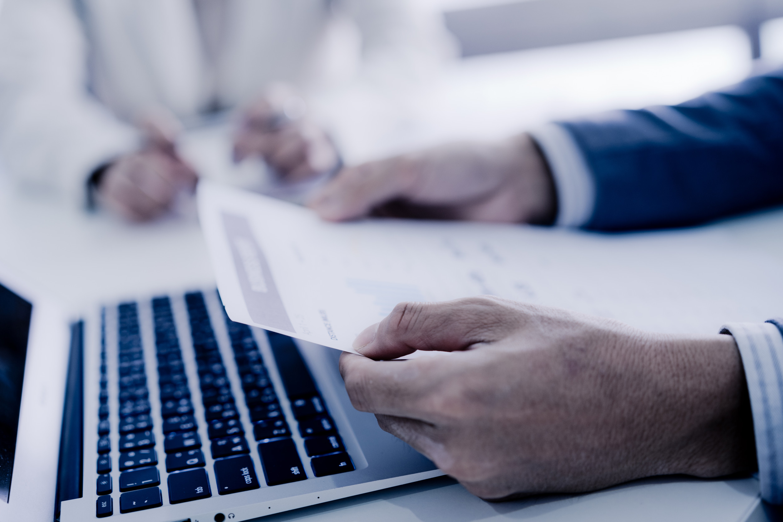 Personne tenant un document près d'un ordinateur portable.